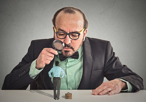 curious corporate businessman skeptically meeting looking at small employee standing on table through magnifying glass isolated office grey wall background. Human face expression, attitude, perception